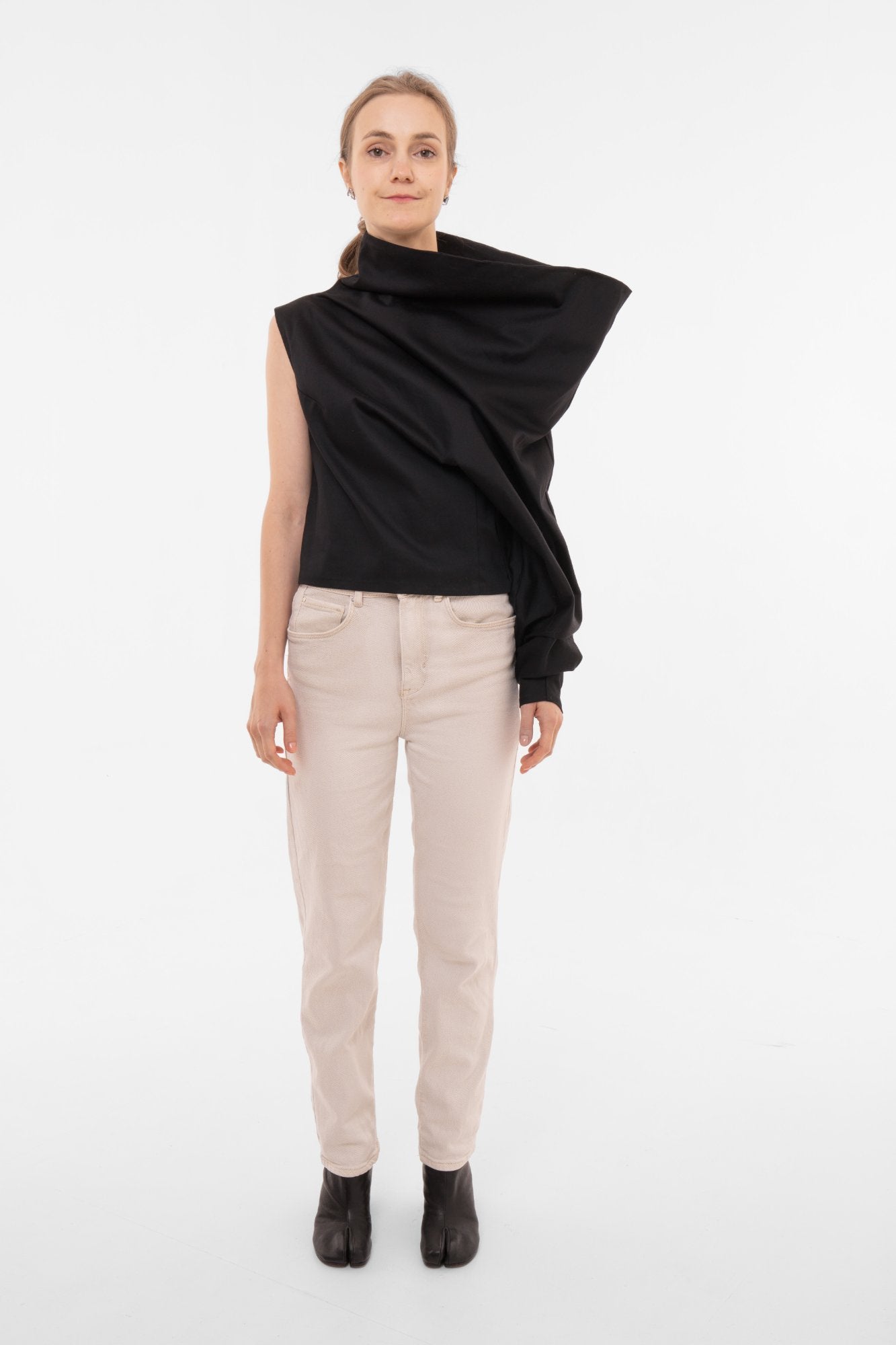 Woman wearing a black draped asymmetrical top and beige pants on a white background