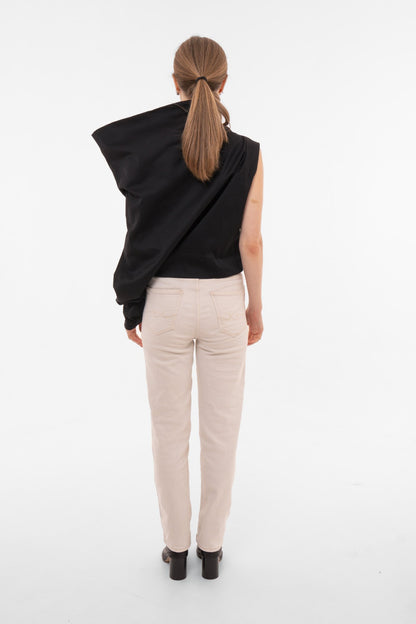 Person wearing a black draped asymmetrical top and beige pants on a white background