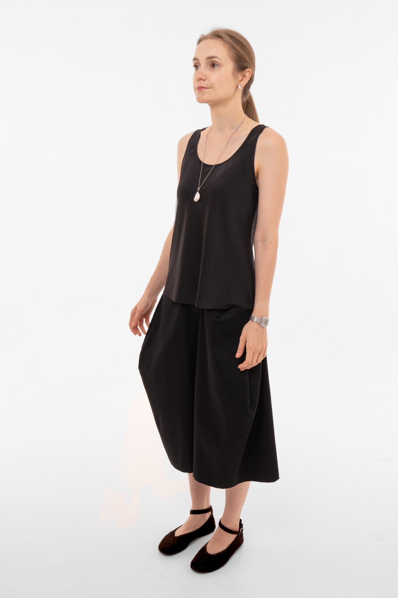Woman wearing a black sleeveless top and wide-leg black culottes on a white background