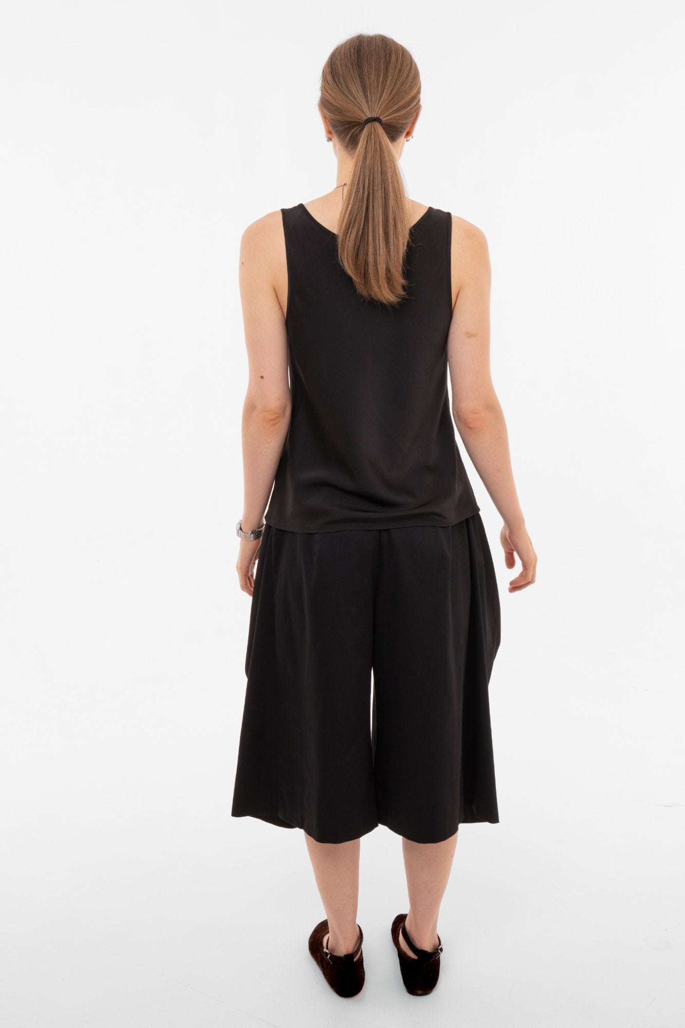 Person wearing a black sleeveless top and black wide-leg pants on a white background, view from behind