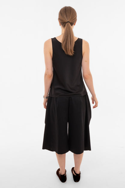 Person wearing a black sleeveless top and black wide-leg pants on a white background, view from behind