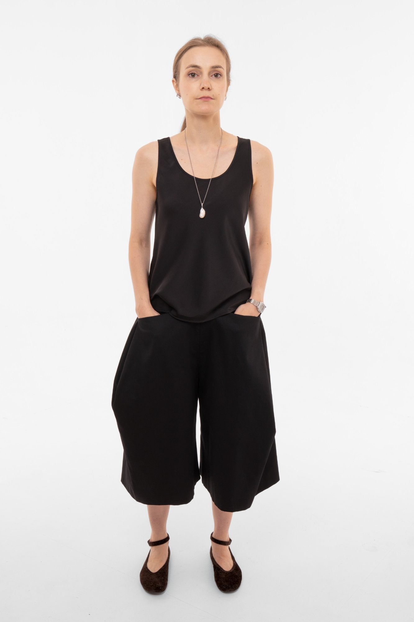 Woman wearing a black sleeveless top and wide-leg black pants on a white background