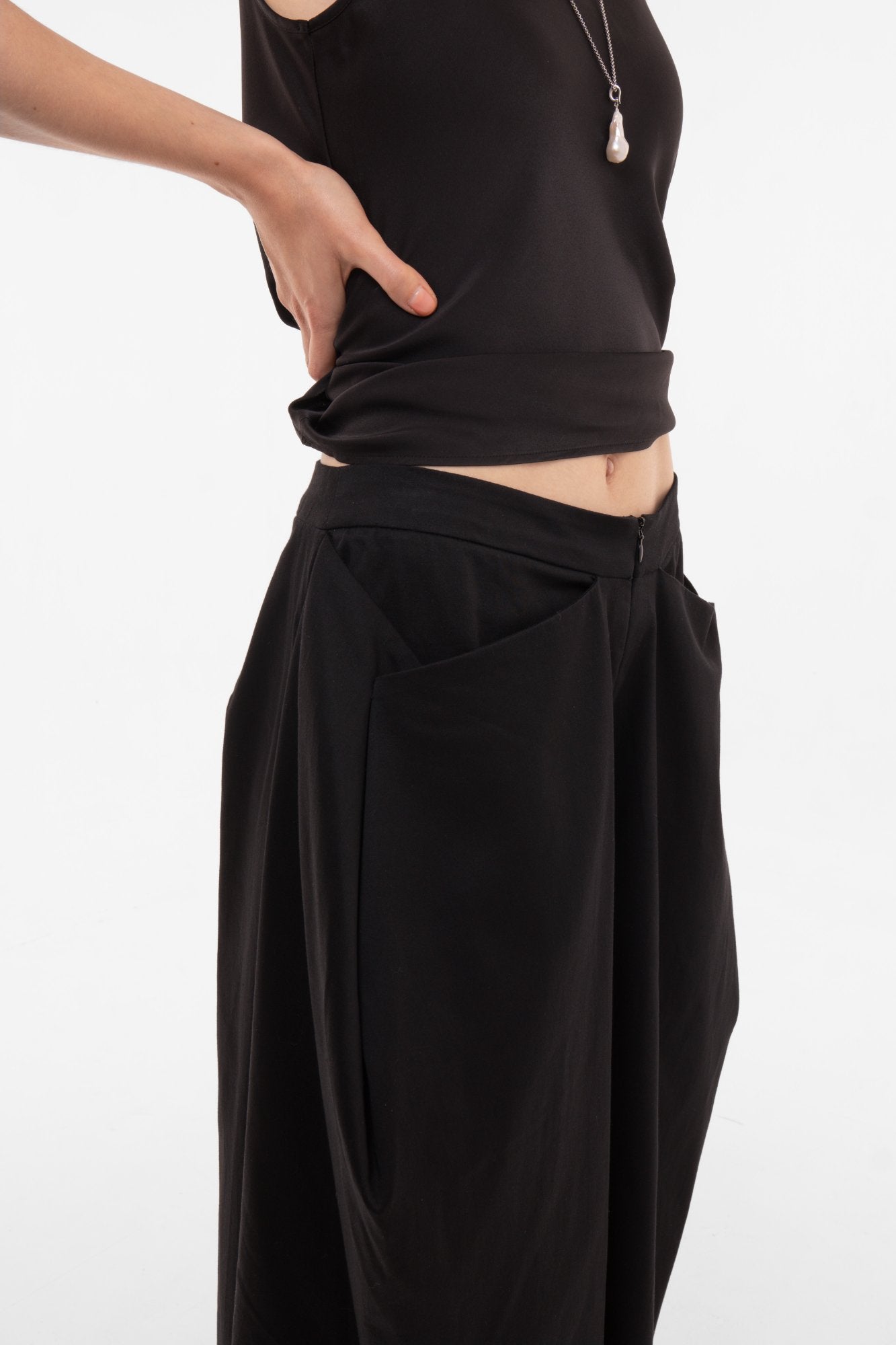 Person wearing a black outfit with a top and black wide-leg pants with geometric origami pockets on a white background
