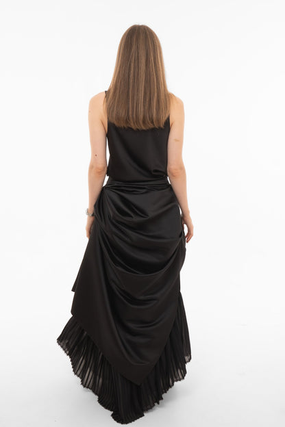 Back view of black maxi skirt with asymmetric draped overlay and pleated hem detail