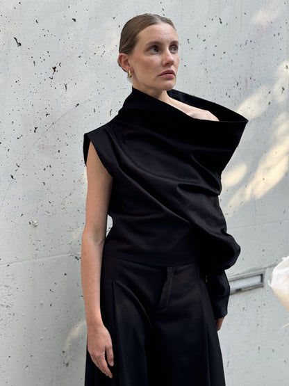 Statement black asymmetric top with dramatic one-shoulder draping, worn with wide-leg pants