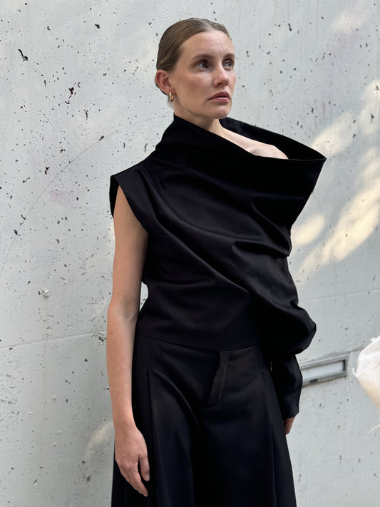 Statement black asymmetric top with dramatic one-shoulder draping, worn with wide-leg pants