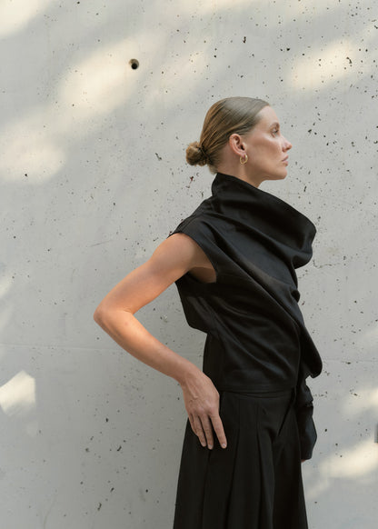 Side profile of a woman wearing a one-shoulder black designer top with bold architectural folds