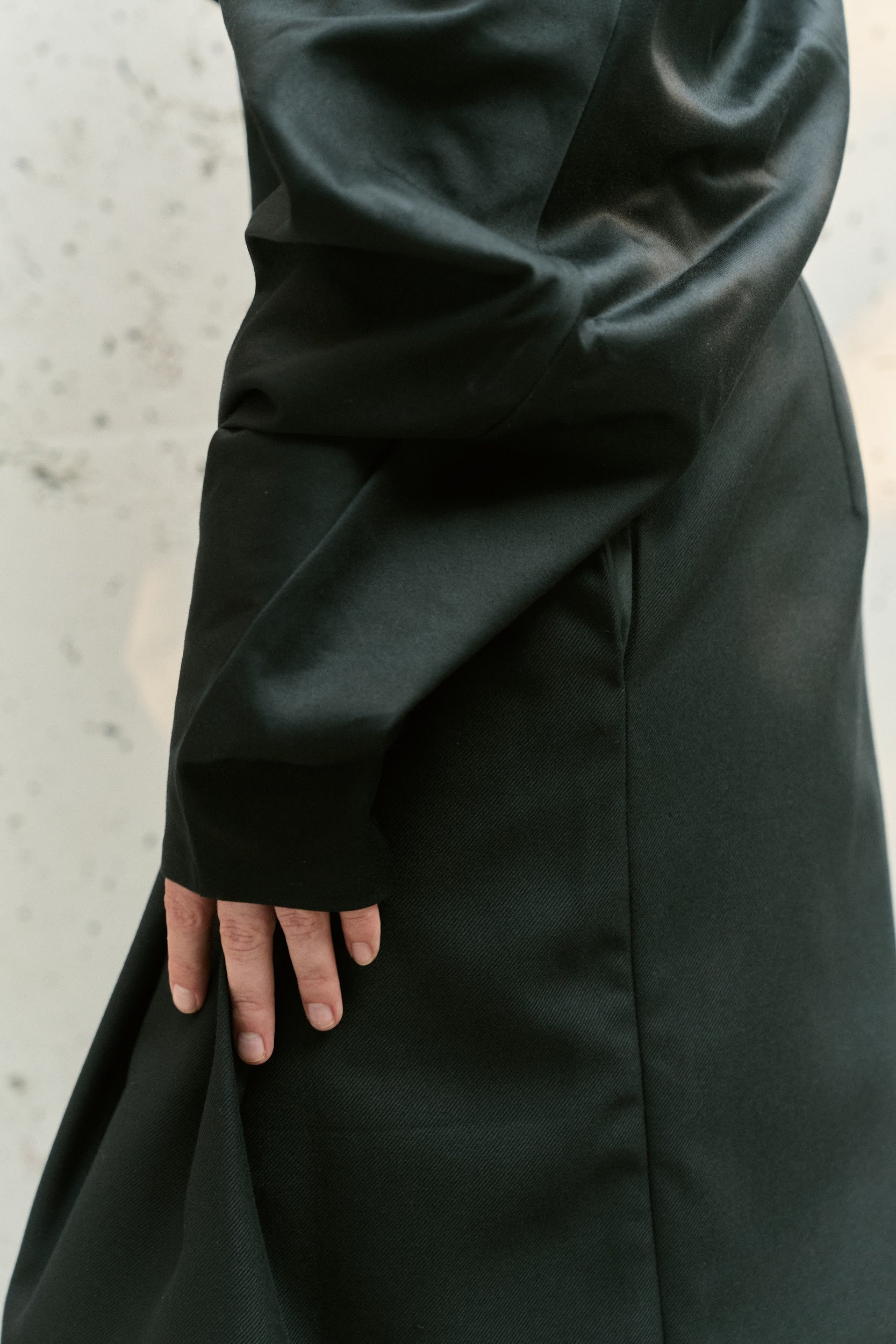Close-up on the long sculptural sleeve and tailored cut of a black asymmetric fashion top