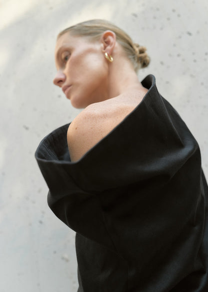 Detailed view of the shoulder draping and matte black fabric texture of the asymmetric sculptural top