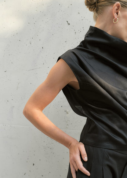Cropped frame highlighting the neckline and folds of a black avant-garde one-shoulder top