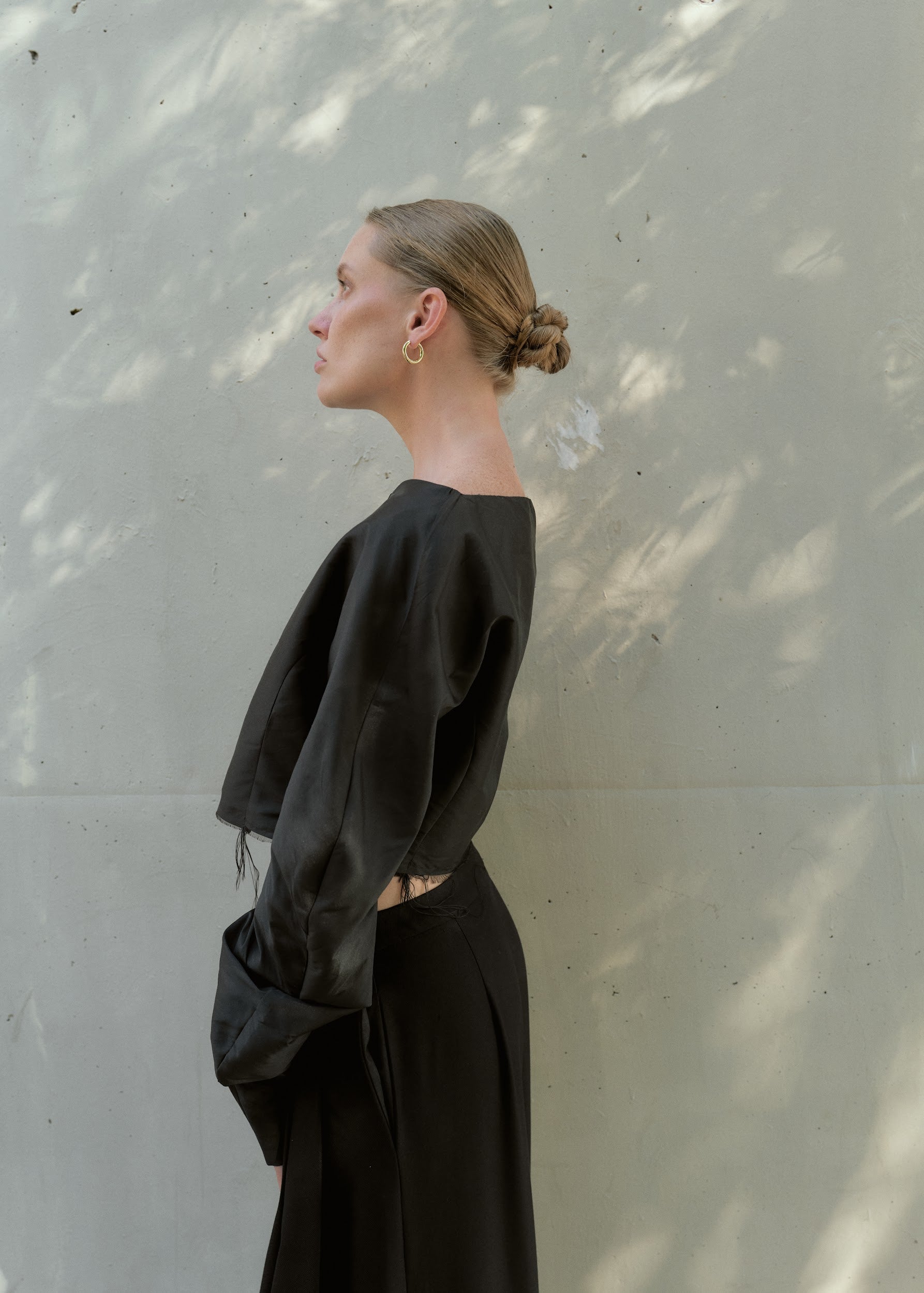 Side profile of a woman wearing a black silk taffeta crop top featuring structured puff sleeves
