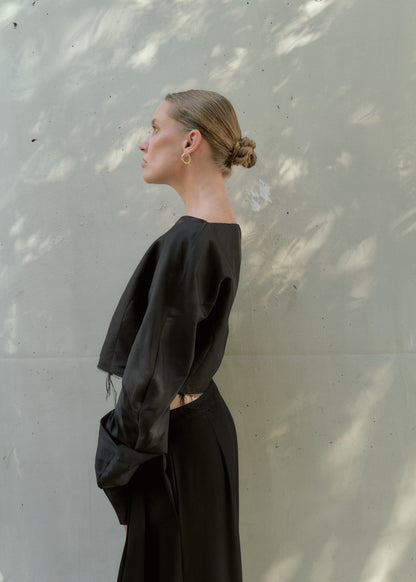 Side profile of a woman wearing a black silk taffeta crop top featuring structured puff sleeves